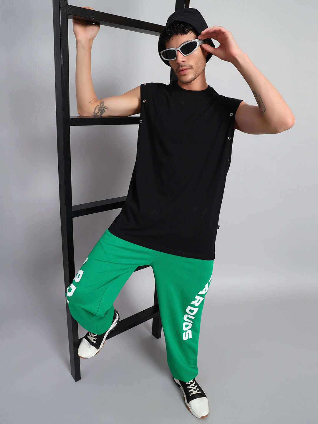 Person wearing ALVEN OVERSIZED T-SHIRT BLACK with sunglasses, striking a pose against a ladder in a modern fashion setting.