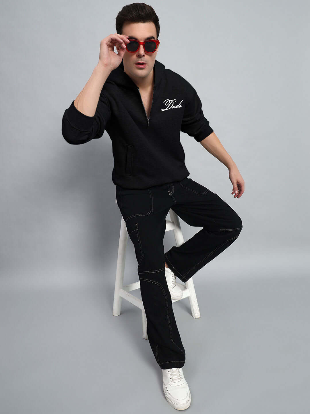 Person wearing WEARDUDS AMARILLO FLEECE HOODIE BLACK sitting on a stool with red sunglasses.