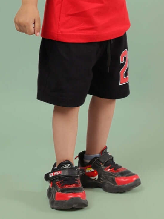 Child wearing AMIGA SHORTS FOR BOYS & GIRLS BLACK RED with red and black sneakers, showcasing sporty style for kids.
