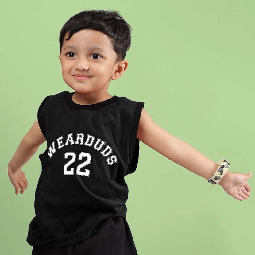 Young child in a black Amiga T-shirt for boys and girls, featuring 'Wearduds 22' text, standing against a green background.