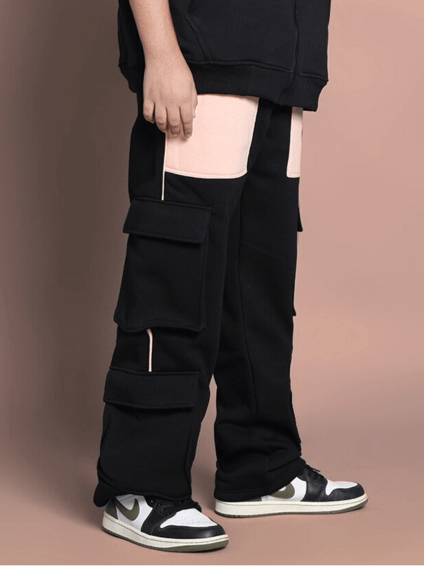Child wearing black-beige fleece jogger with angel wings design, showcasing cargo pockets and stylish sneakers on a brown background.