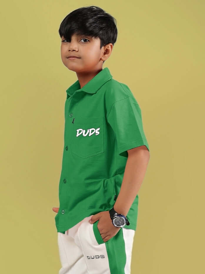 Boy wearing green 'Angry Sponge' shirt by DUDS, hands in pockets, yellow background.