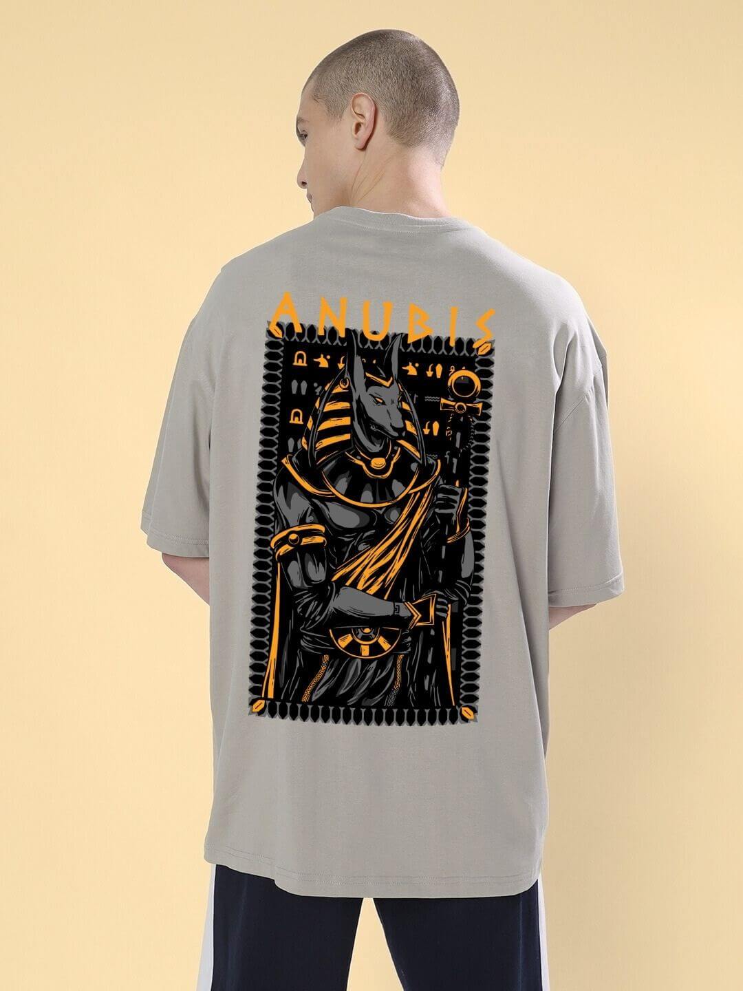 Person wearing ANUBIS EGYPTIAN PRINTED OVERSIZED T-SHIRT GREY with detailed Anubis artwork on the back.