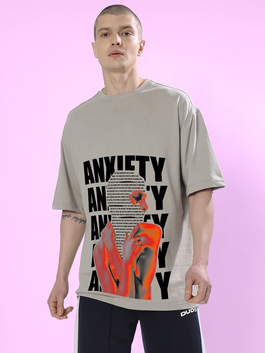 Man wearing ANXIETY OVER-SIZED T-SHIRT GREY with artistic design on the front, standing against a purple background.
