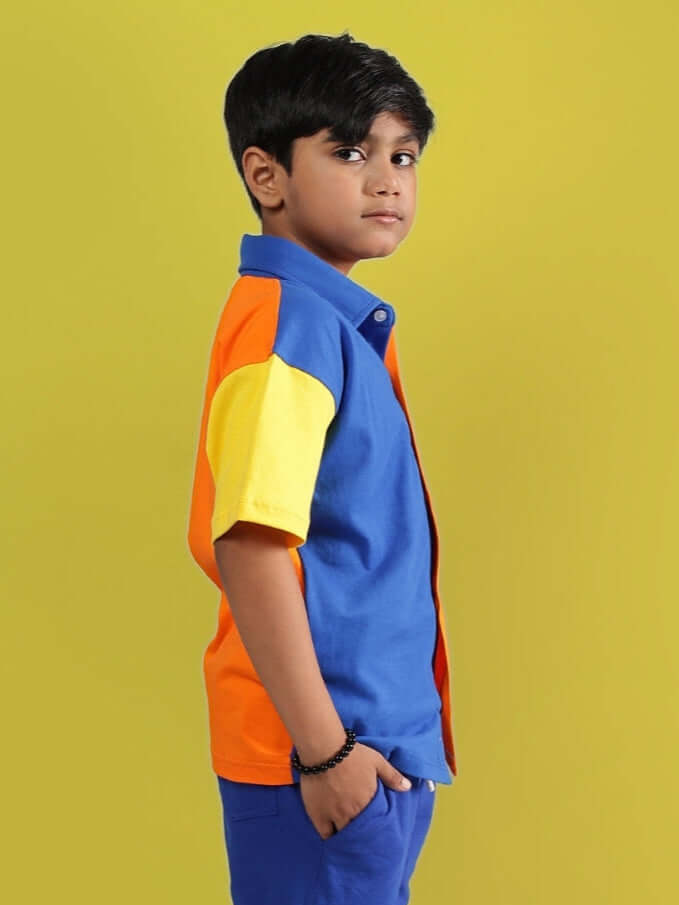 Young boy wearing a multi-blue APEX shirt, standing against a yellow background, showcasing the vibrant and stylish design for kids.