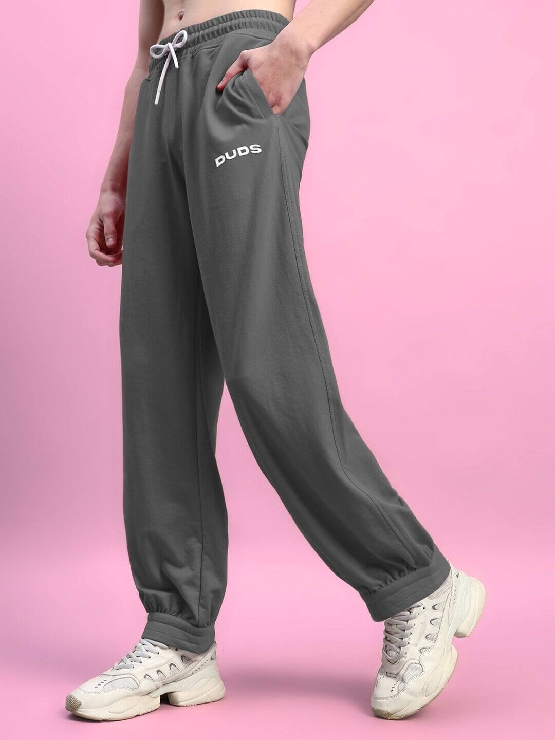 Person wearing Austrian relaxed-fit grey joggers from DUDS on a pink background.