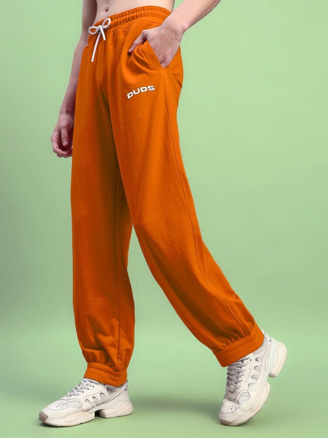 Model wearing Austrian relaxed-fit joggers in orange by DUDS, showcasing comfortable and stylish fit.