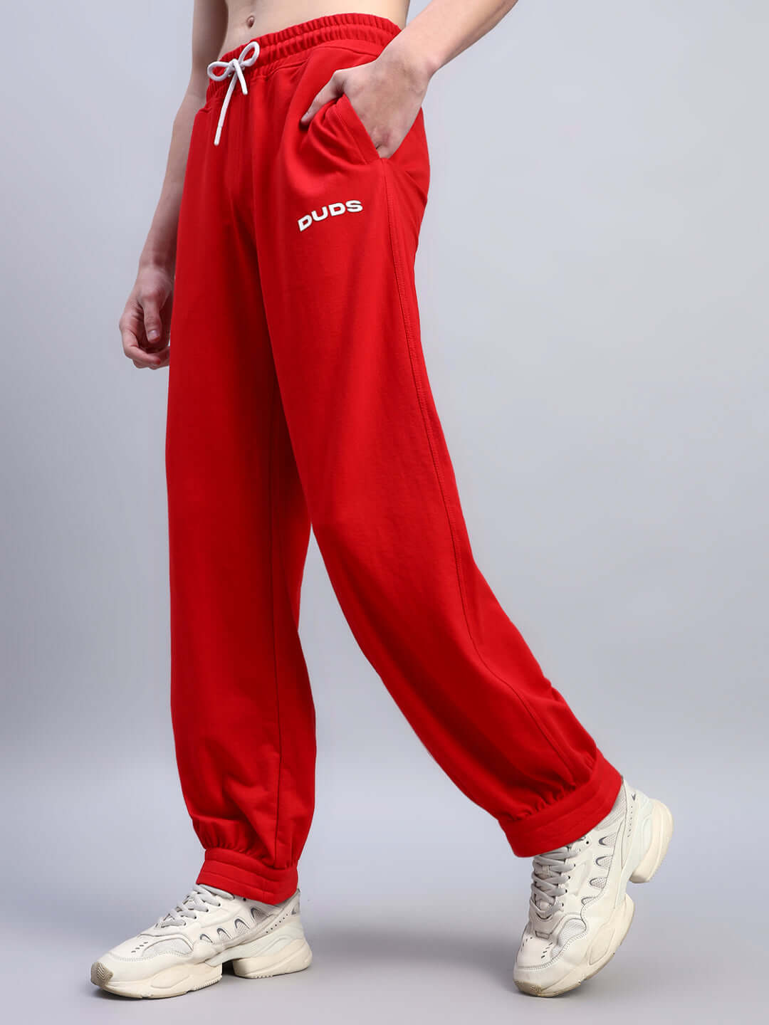 Person wearing red relaxed-fit joggers with DUDS logo, showcasing comfortable fit and elastic cuffs, paired with white sneakers.