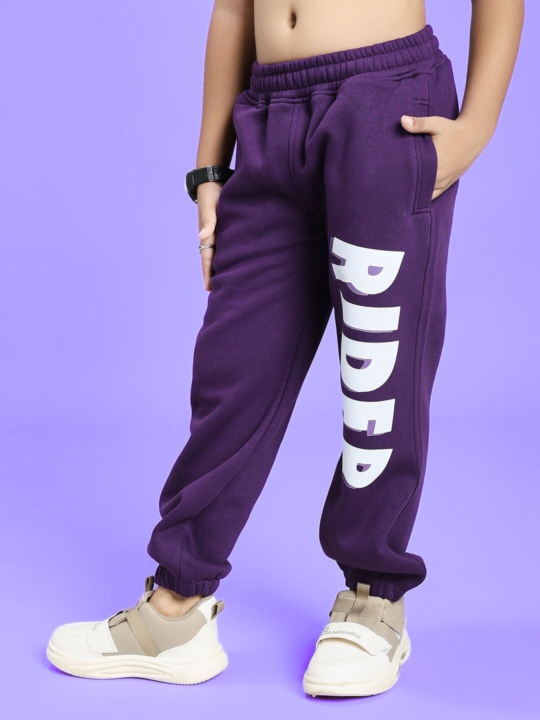 Child wearing AUTHENTIC RIDER FLEECE JOGGER FOR BOYS AND GIRLS PURPLE with white sneakers on purple background