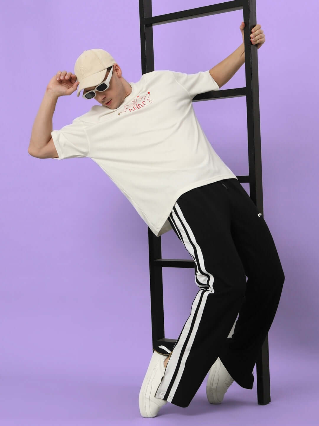 Model wearing Avalon Slit Zipper Joggers in black and white, styled with a casual tee and cap, leaning against a ladder.