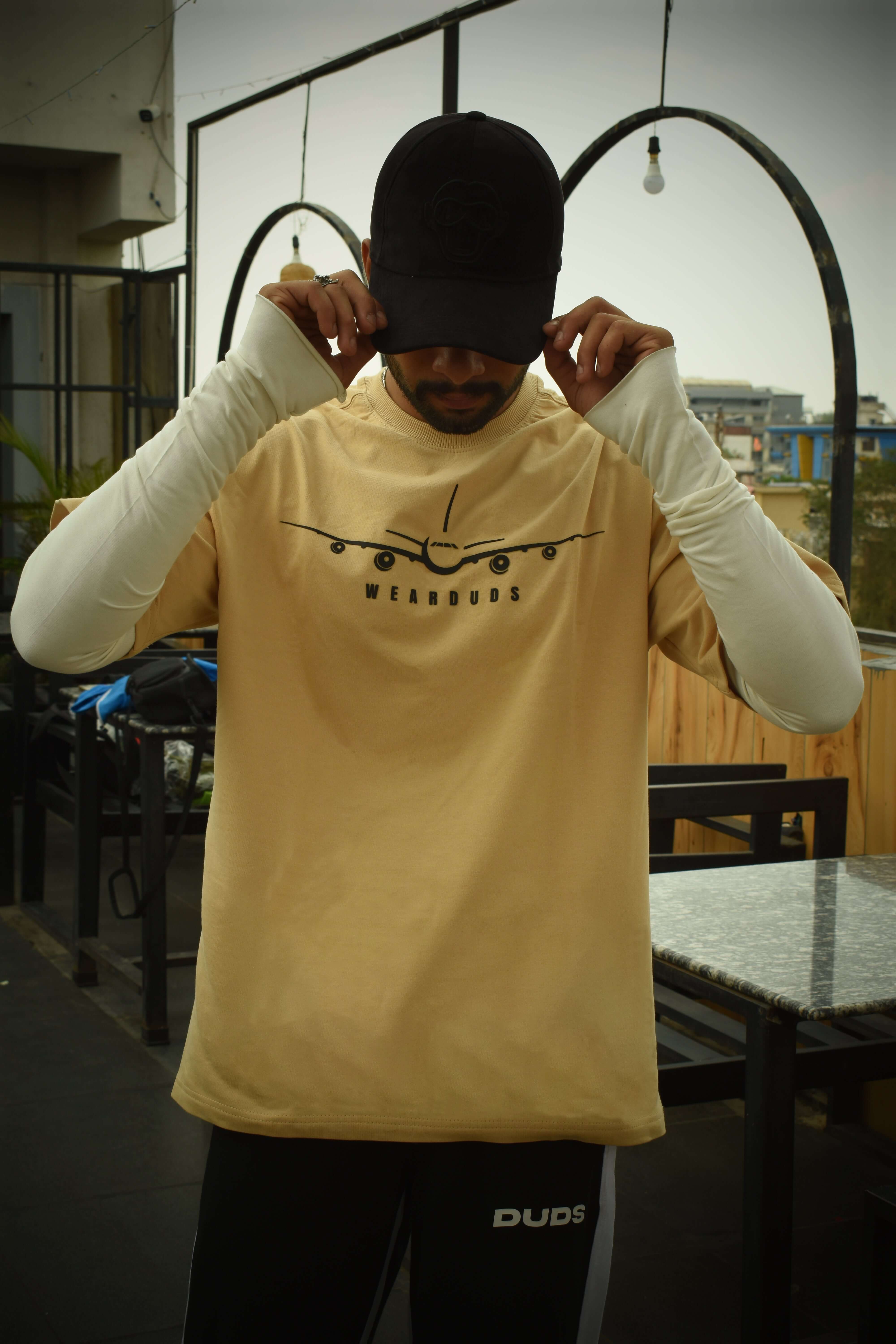 Model wearing a beige over-sized Aviator designer t-shirt made from premium cotton fabric, featuring aviation graphic, outdoor setting.