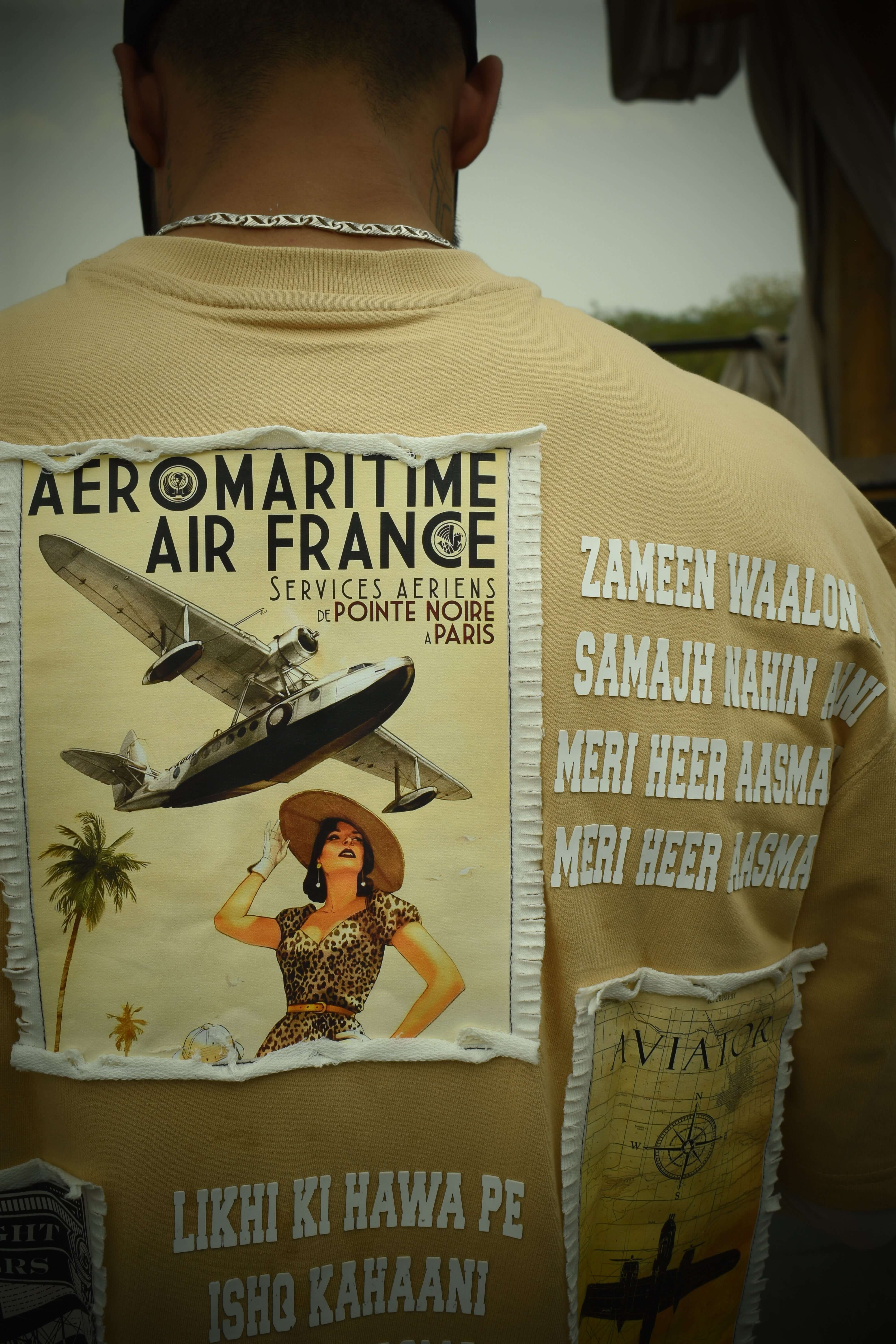 Back view of an oversized beige Aviator designer t-shirt with vintage aeronautical patch and text details.