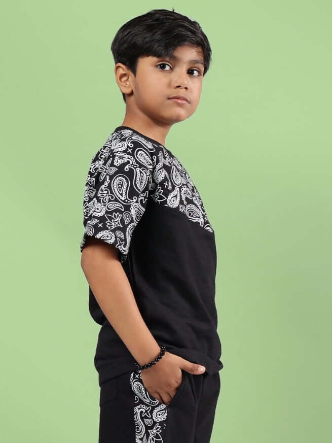 Child wearing Baladeer oversized t-shirt for boys & girls in black, featuring paisley design on sleeves, standing against a green background.