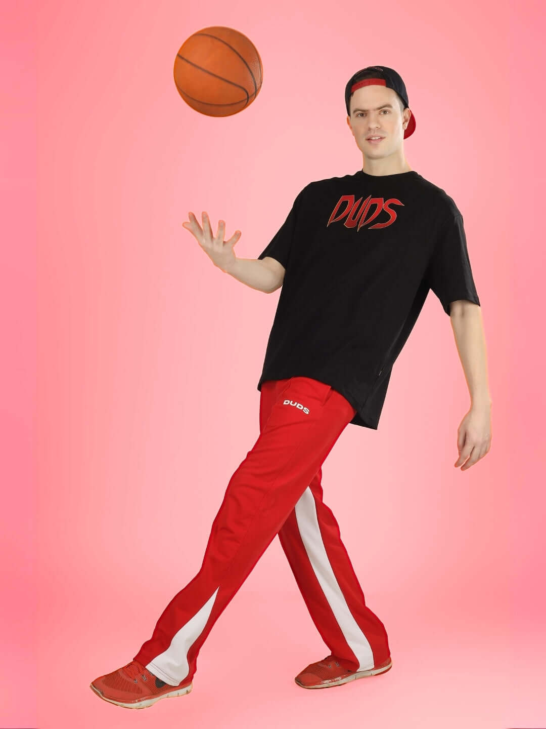 Man wearing Mafia oversized black t-shirt by DUDS, playing basketball, styled with red athletic pants and sneakers.