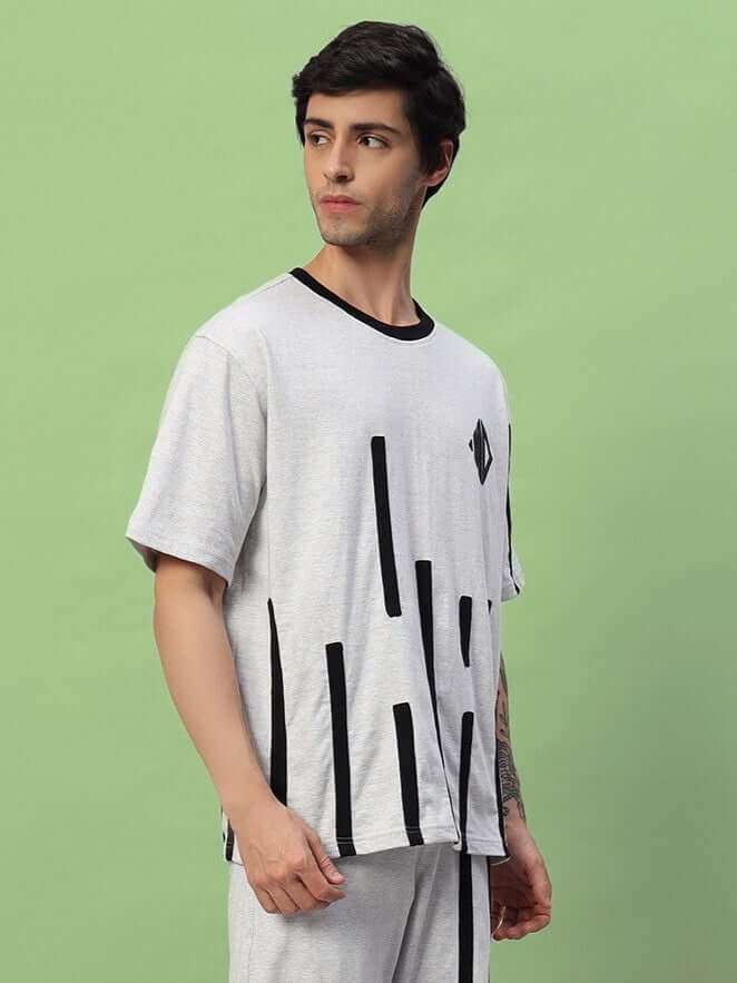 Man wearing Bastille Oversized T-Shirt Melange Grey with modern design, featuring relaxed fit and minimalistic style, set against a green background.