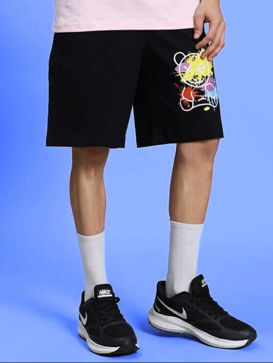 Model wearing BE KIND REGULAR FIT SHORTS BLACK with colorful design, showcasing stylish and comfortable fit on a bright background.