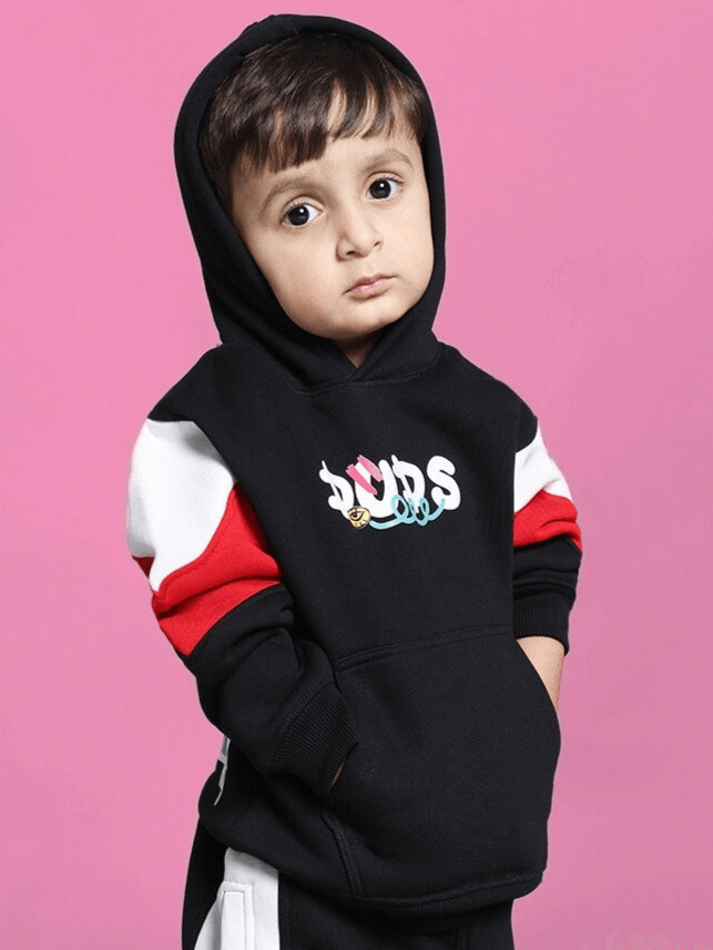 Child wearing a black beanie hoodie with colorful DUDS logo and red, white sleeves, against pink background. Made-to-order by experienced tailors.