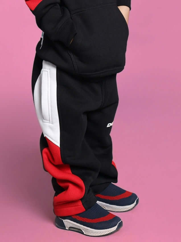 Child wearing black, red, and white beanie hoodie with matching pants on pink background