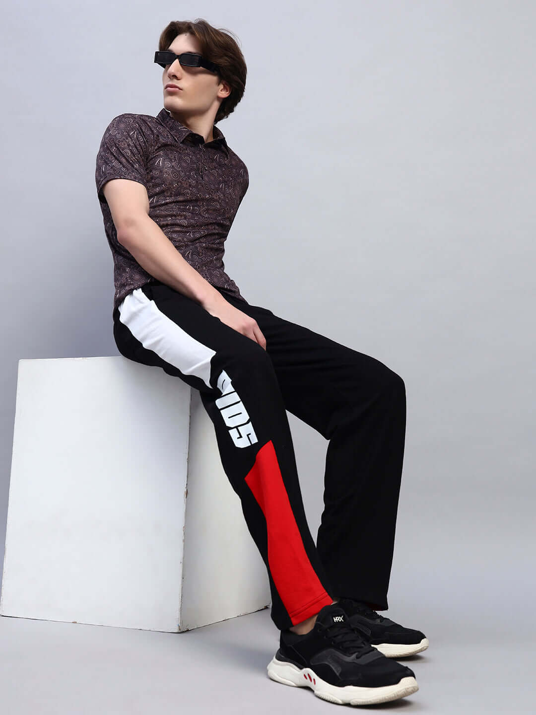 Model wearing Belgians relaxed-fit joggers in black and red, seated casually, showcasing stylish comfort.