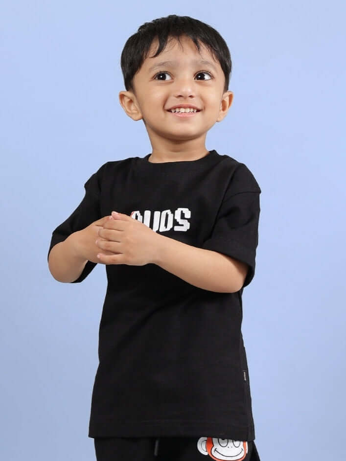 Young child wearing a black BINGO T-shirt for boys and girls by DUDS, smiling against a light blue background.