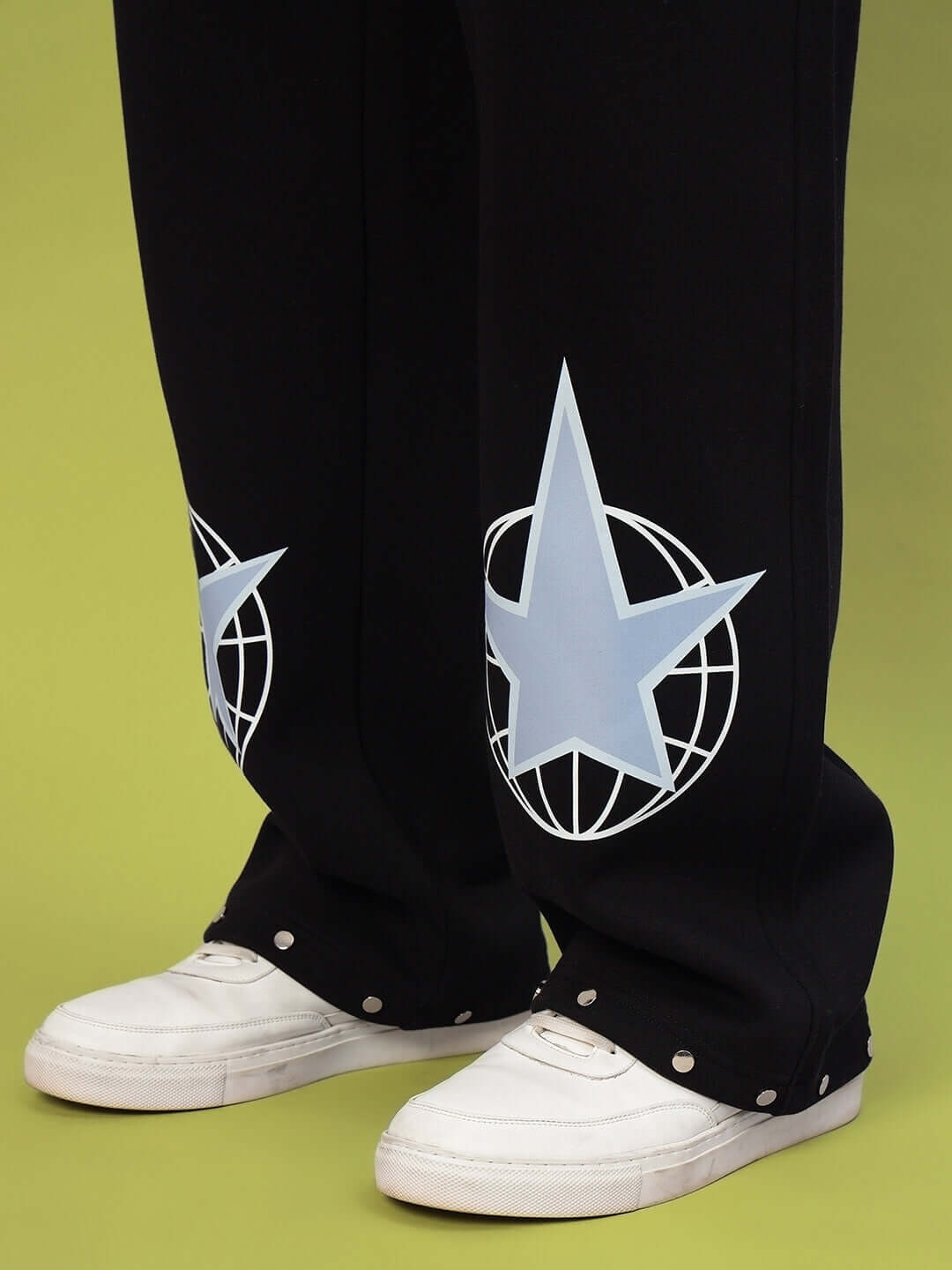 Black cotton fleece joggers with star design detail, paired with white sneakers on a green background.