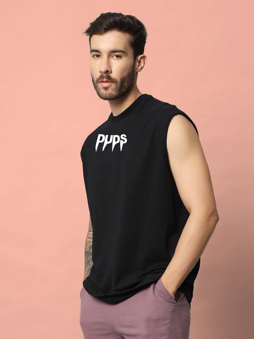 Person wearing a black sleeveless gym t-shirt with 'Pups' logo, standing against a pink background.