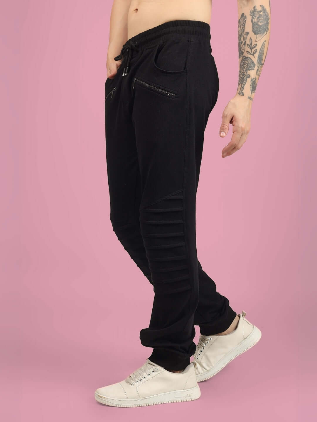 Side view of black jogger pants with 2 zipper pockets and ribbed knee detail, modeled on pink background.
