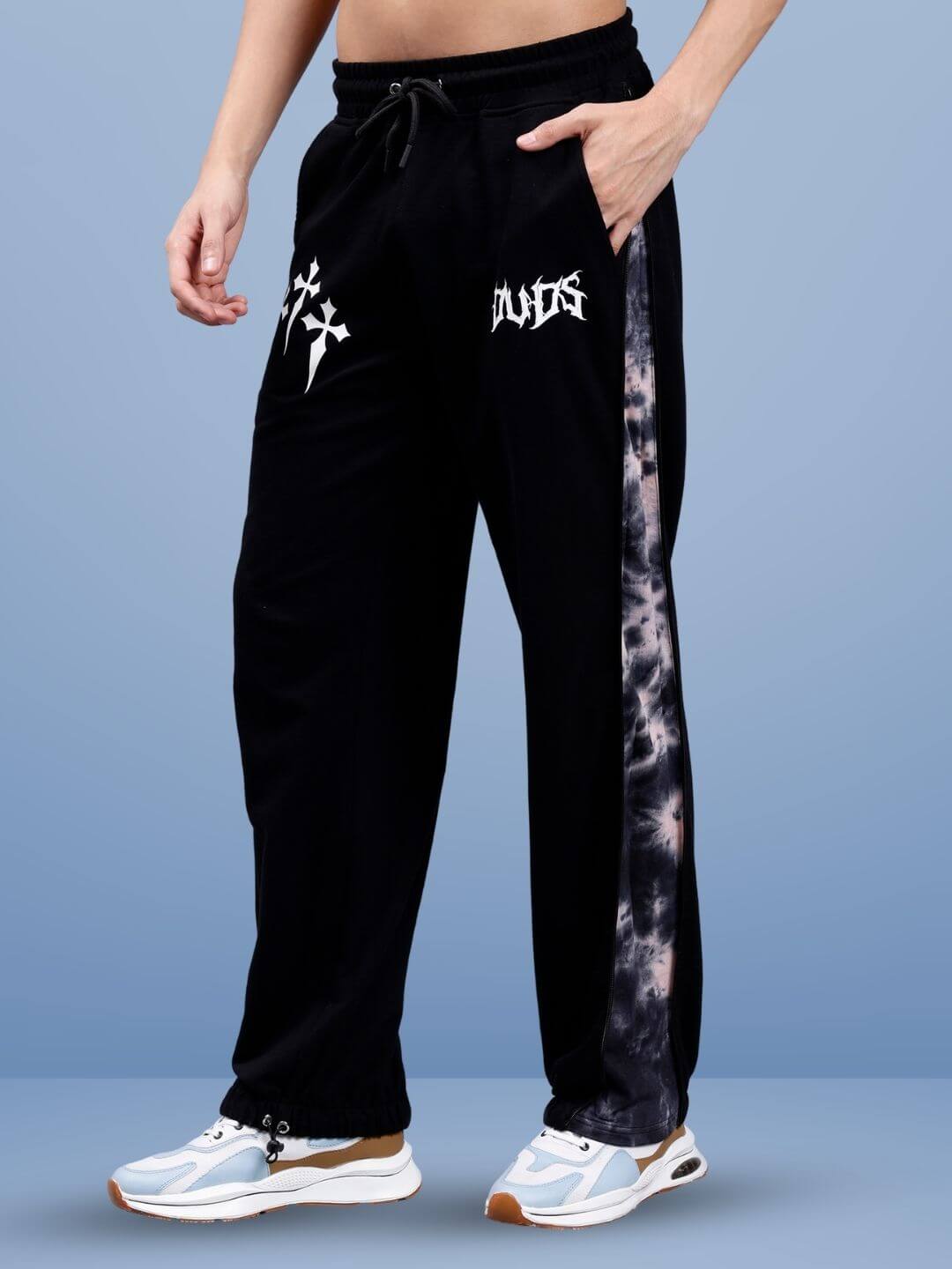 Black joggers with unique patterns and drawstring waist, worn with white sneakers on a blue background.