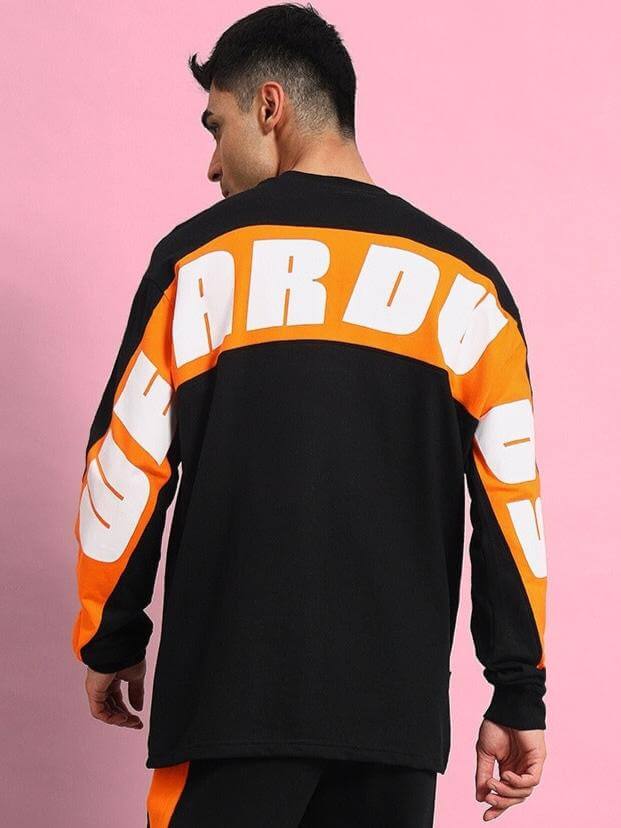 Back view of a person wearing a black oversized co-ord set with bold orange and white lettering on the sleeves and back.