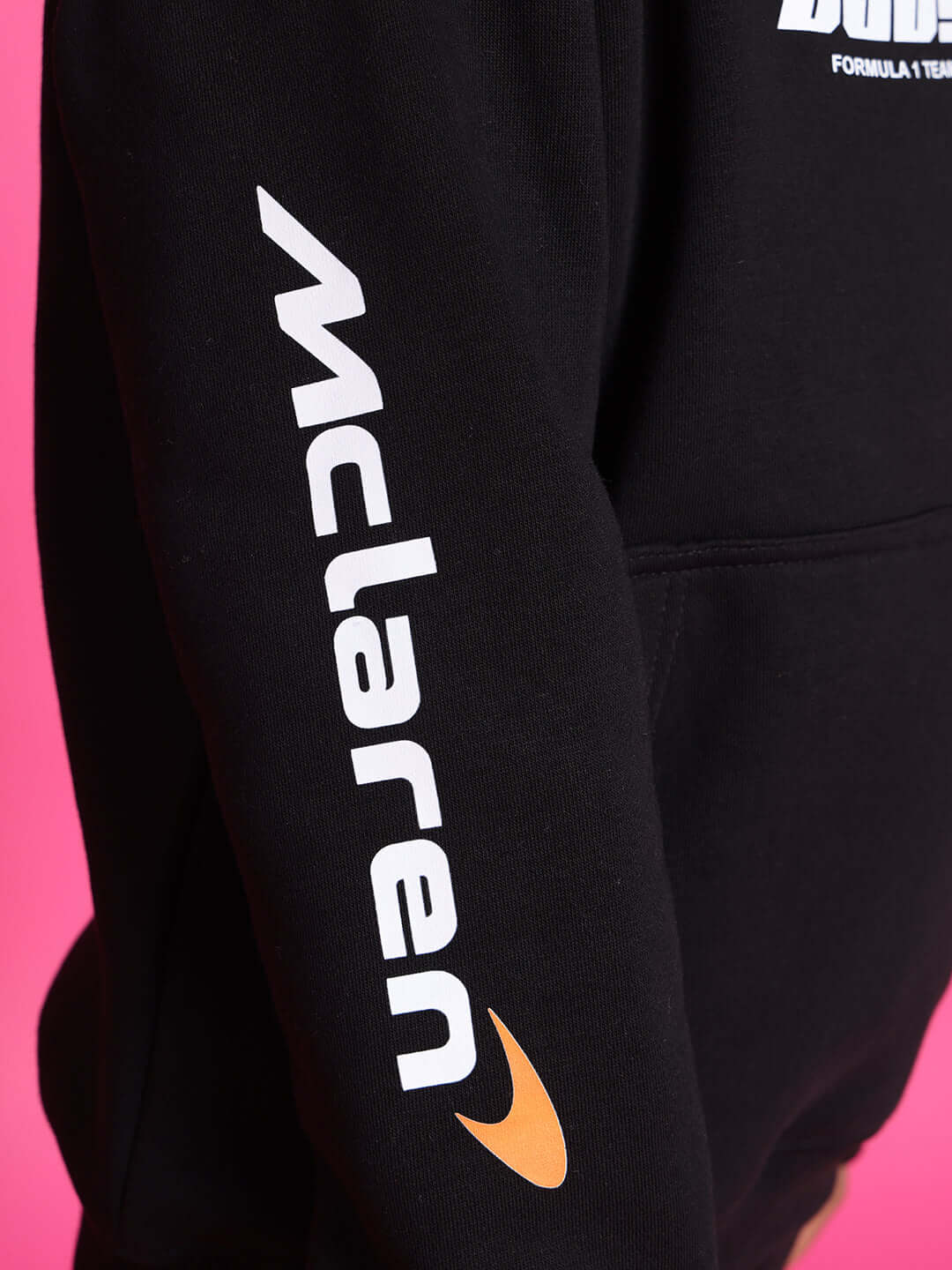 Close-up of sleeve on black hoodie with McLaren logo against a pink background.