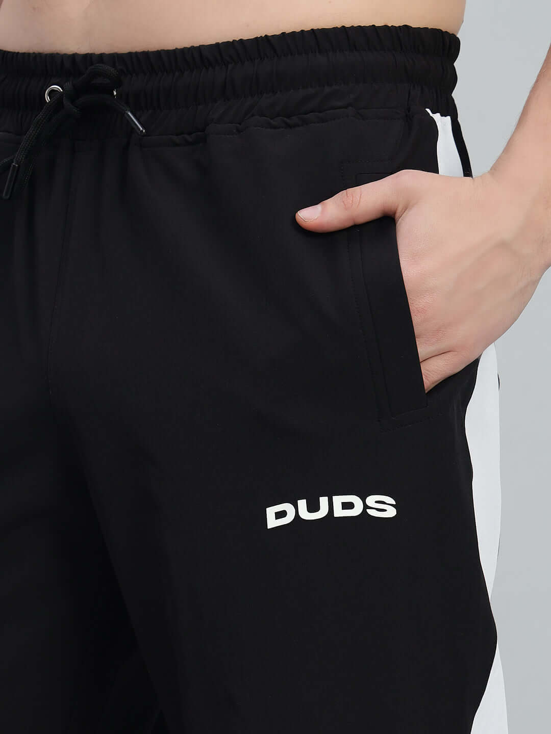 Close-up of black athletic pants with white 'DUDS' logo and side stripes, highlighting pocket detail and relaxed fit design.