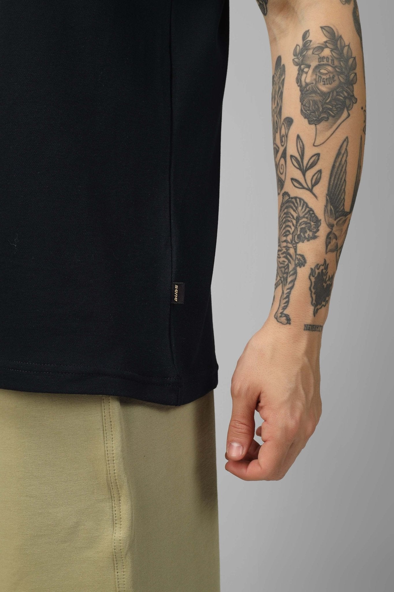 Side view of a model wearing a ZIPPER POLO NECK ZIPPER T-SHIRT BLACK with visible tattoos and light pants.
