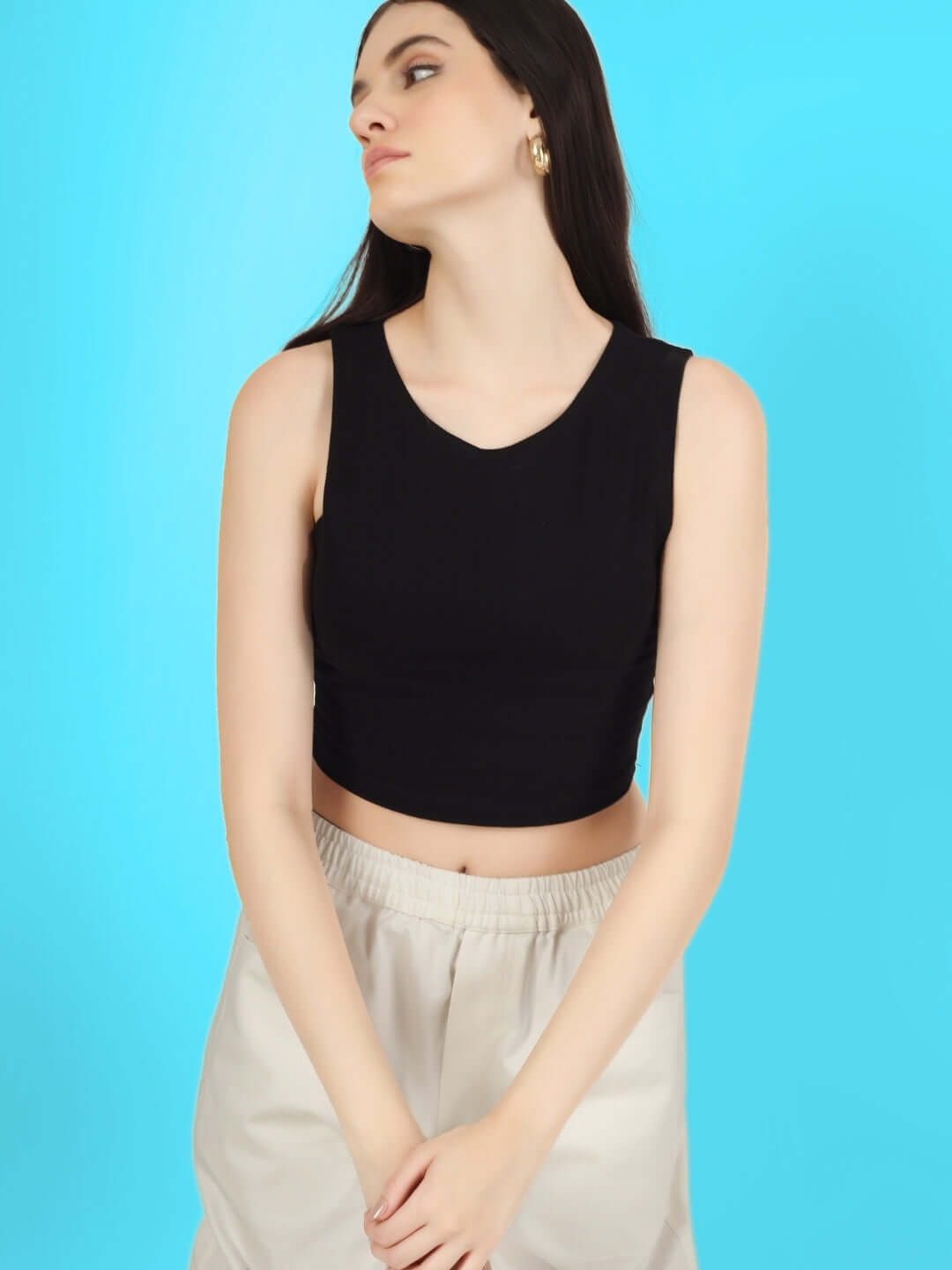 Model wearing a black sleeveless crop top and cream pants against a blue background.