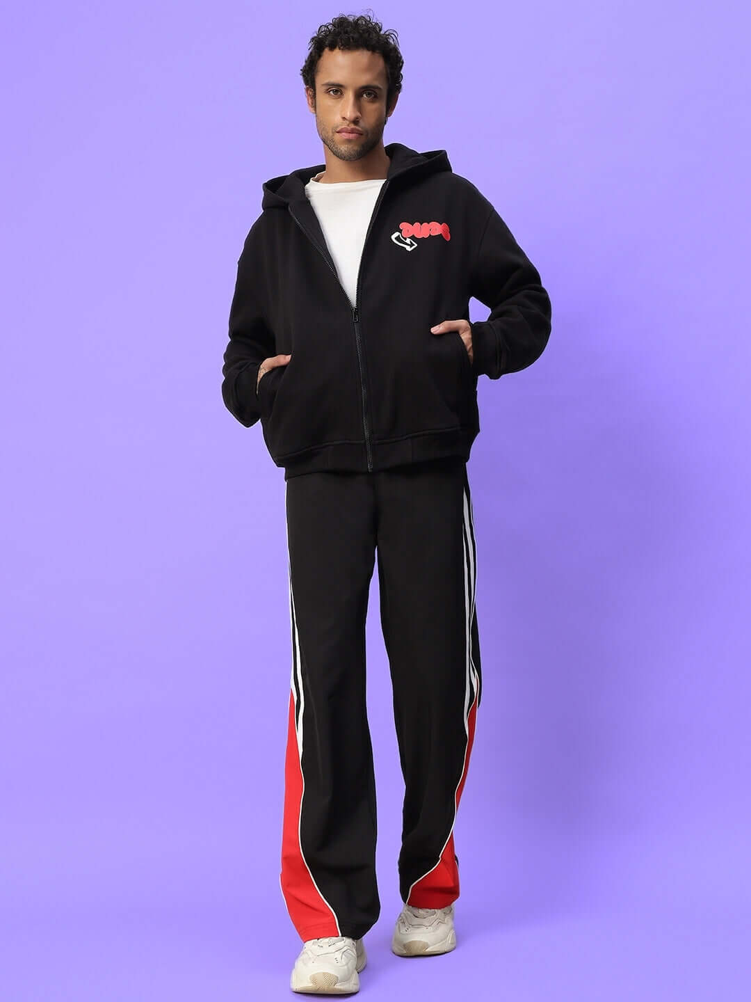 Model wearing black and red sporty tracksuit with a casual stance against a purple background