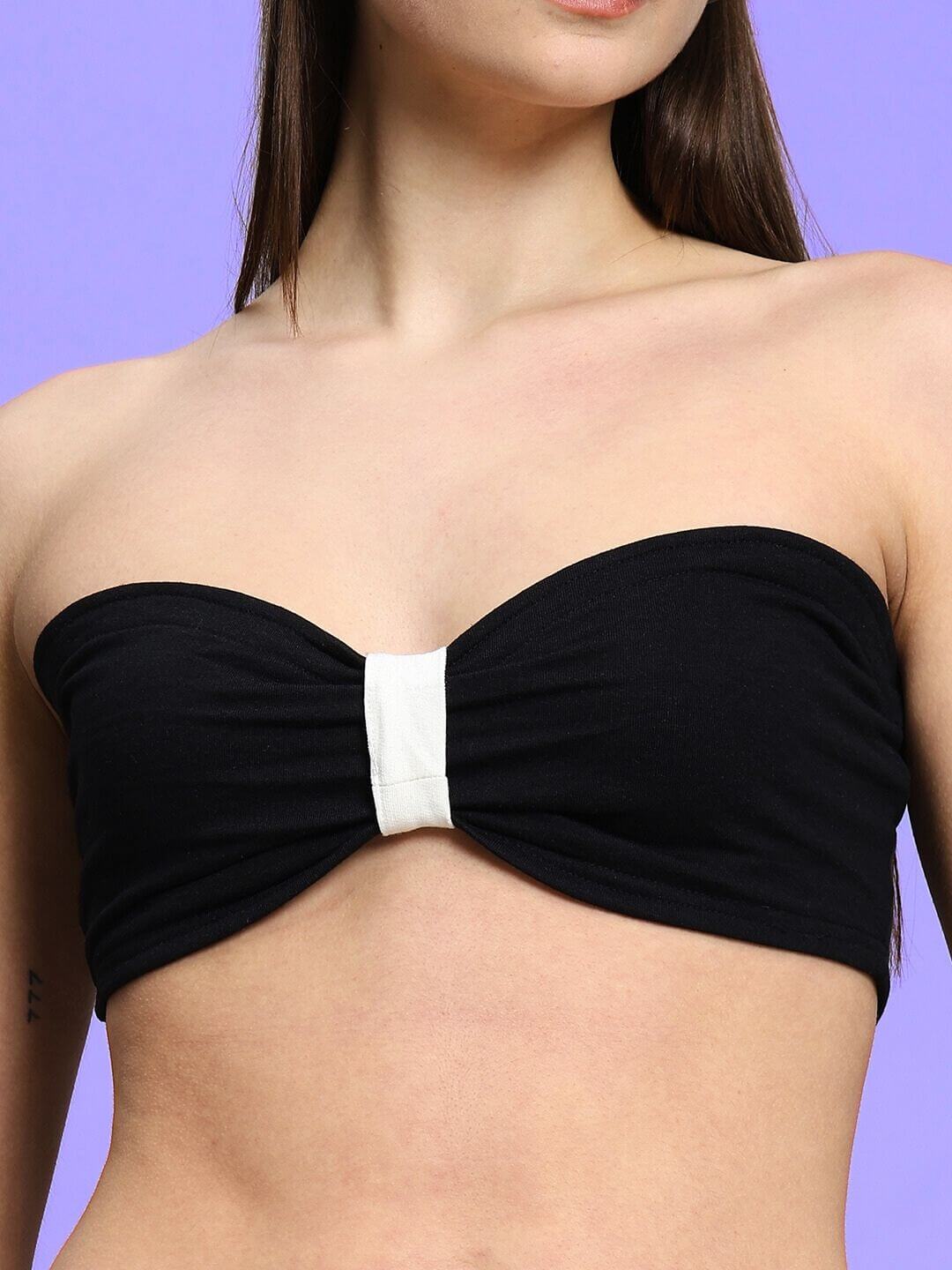 Woman wearing a black strapless bandeau top with white center detail against a purple background.