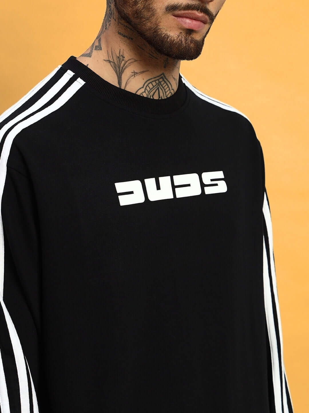 A person wearing a black sweatshirt with white stripes and a white logo, set against an orange background.