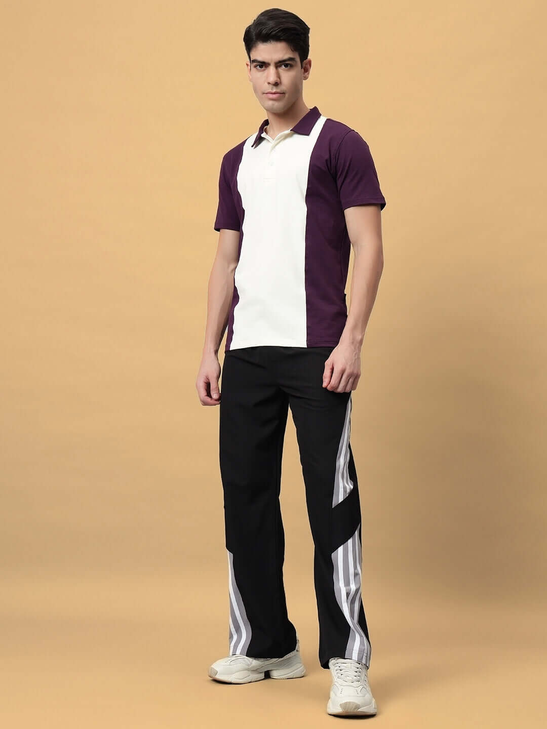 Man wearing black cargo pants and a purple and white polo, standing on a tan background.