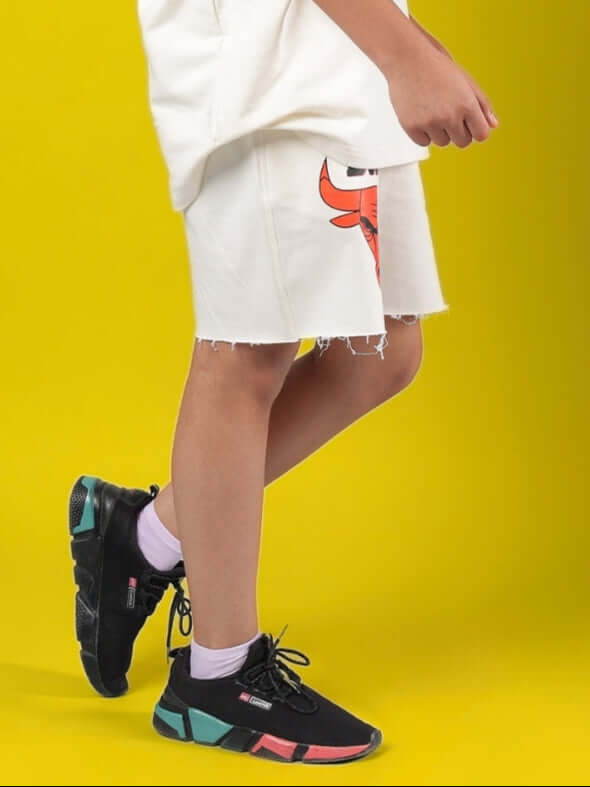 BLAZE BULLS SHORTS FOR BOYS & GIRLS OFF-WHITE displayed on a child, highlighting the casual style against a vibrant yellow background.