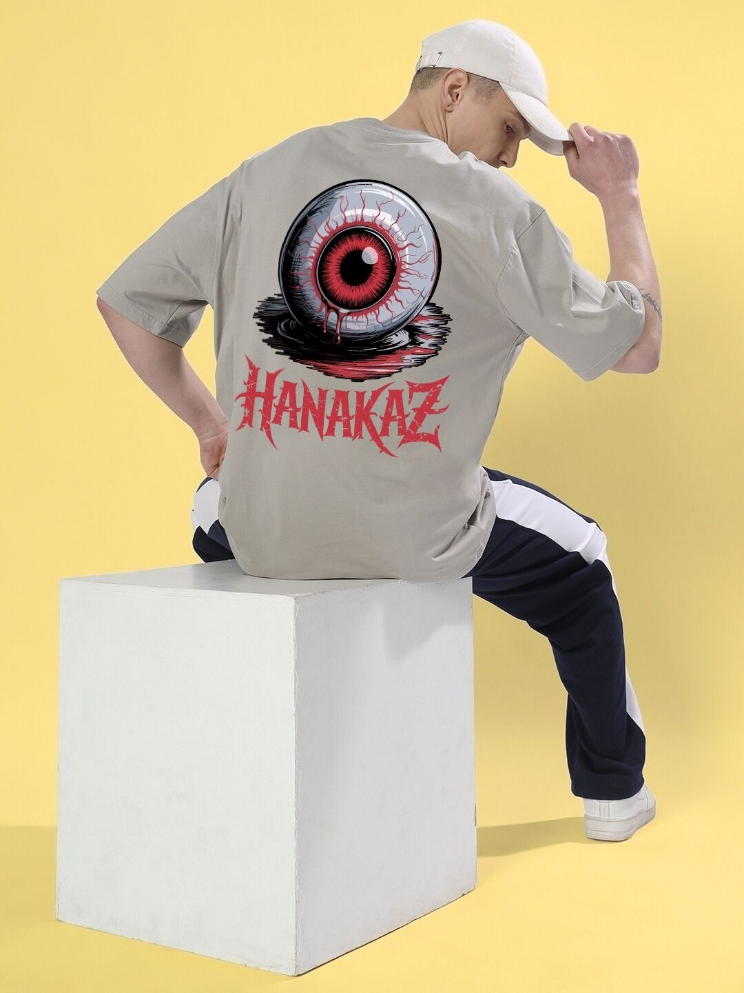Man wearing BLOODY EYE OVER-SIZED T-SHIRT GREY with graphic design sitting on a block in a studio setting.