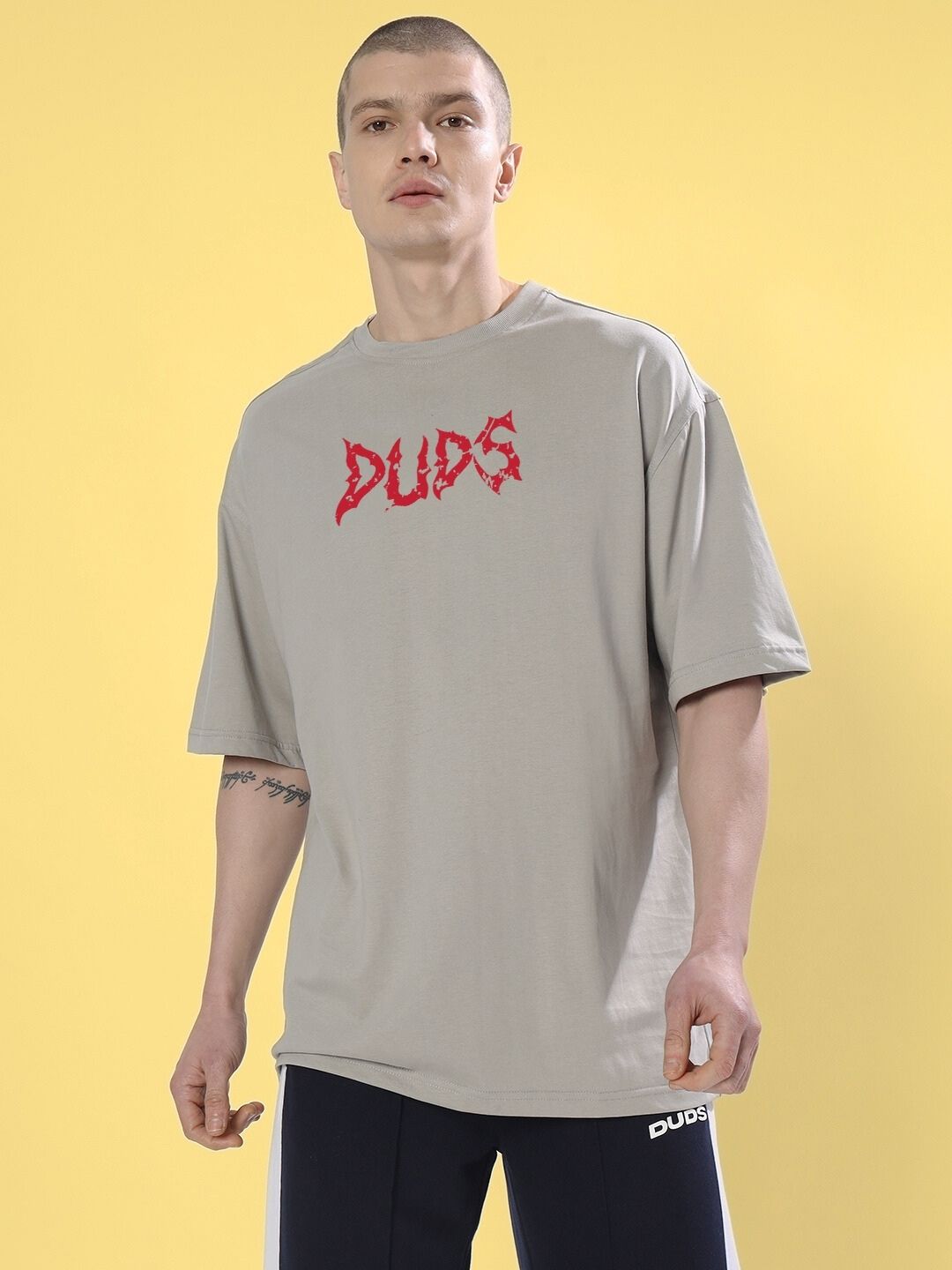 Model wearing BLOODY EYE OVER-SIZED T-SHIRT GREY with bold design on a yellow background.