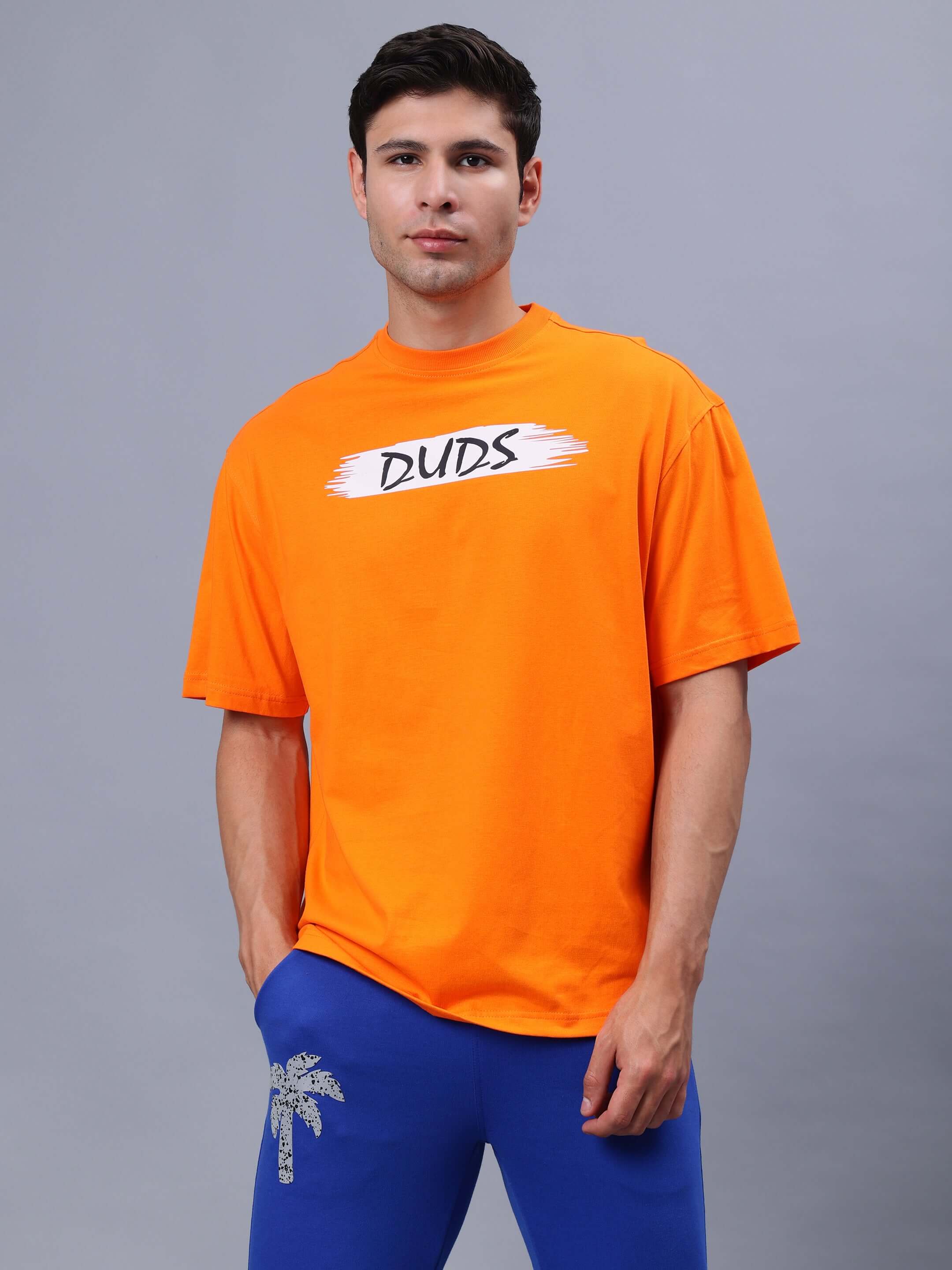 Model wearing orange BLOOM QUOTE oversized T-shirt from DUDS, featuring custom fit options, against a gray background.