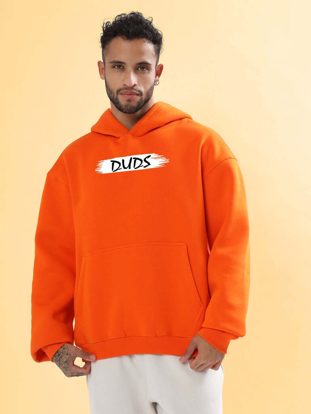 Man wearing BLOOM QUOTE FLEECE OVERSIZED HOODIE ORANGE standing against a yellow background.