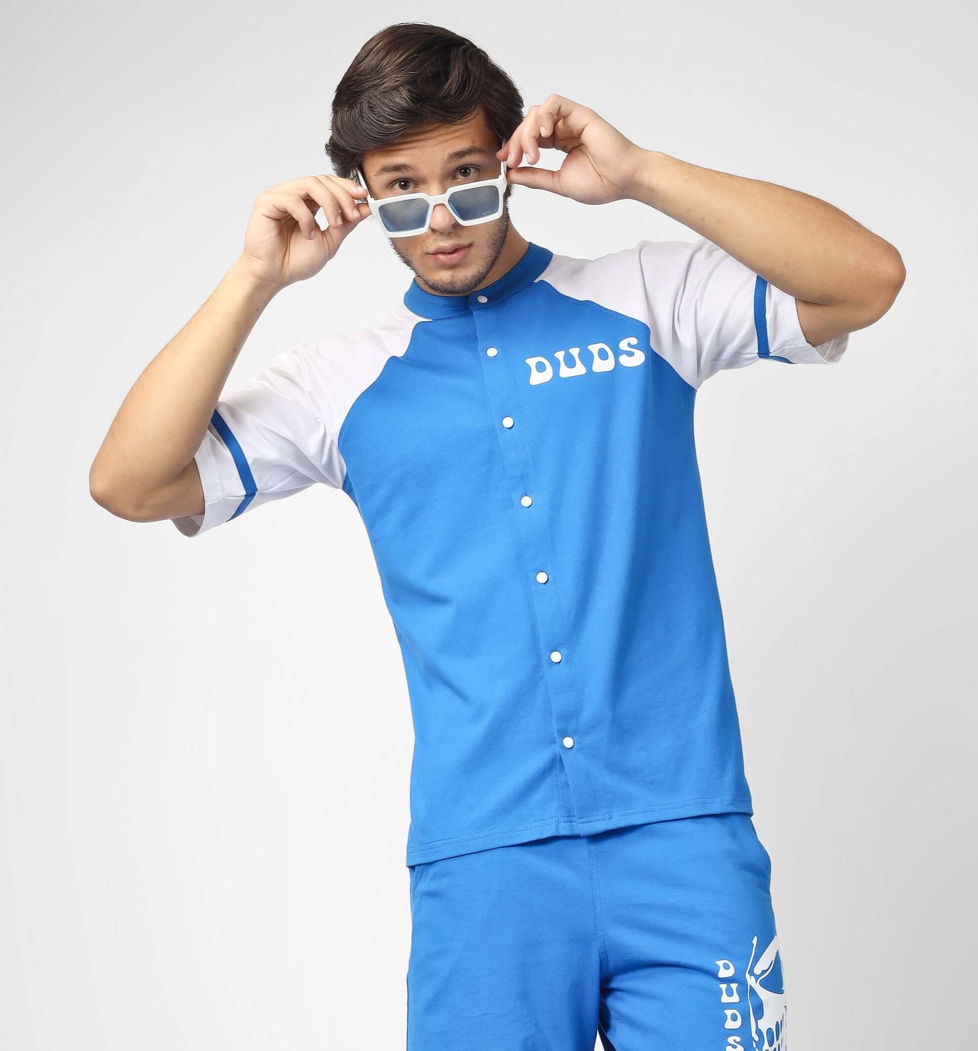 Person in blue Duds shirt and shorts posing with sunglasses.