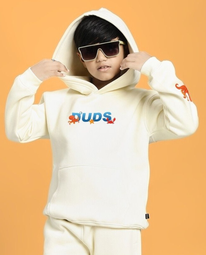 Child wearing BLUE OCEAN WORLD FLEECE HOODIE FOR BOYS AND GIRLS OFF-WHITE with graphics, holding hood and wearing sunglasses.