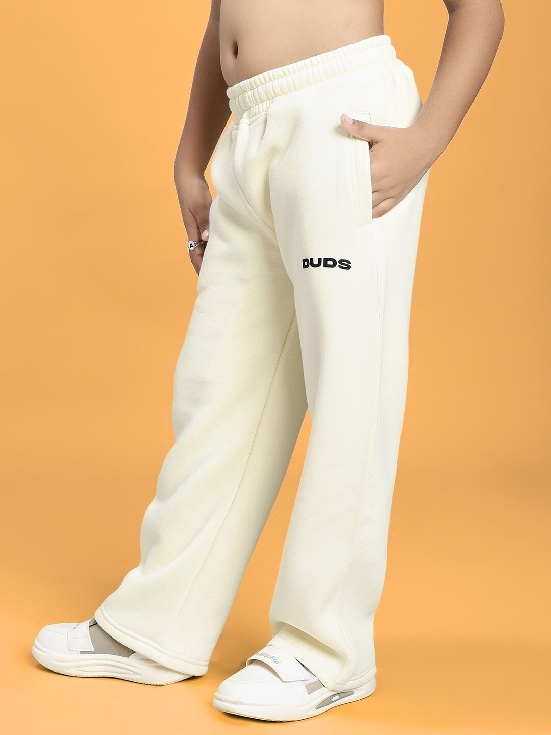 Child wearing BLUE OCEAN WORLD FLEECE JOGGER FOR BOYS AND GIRLS OFF-WHITE with hands in pockets and white sneakers.
