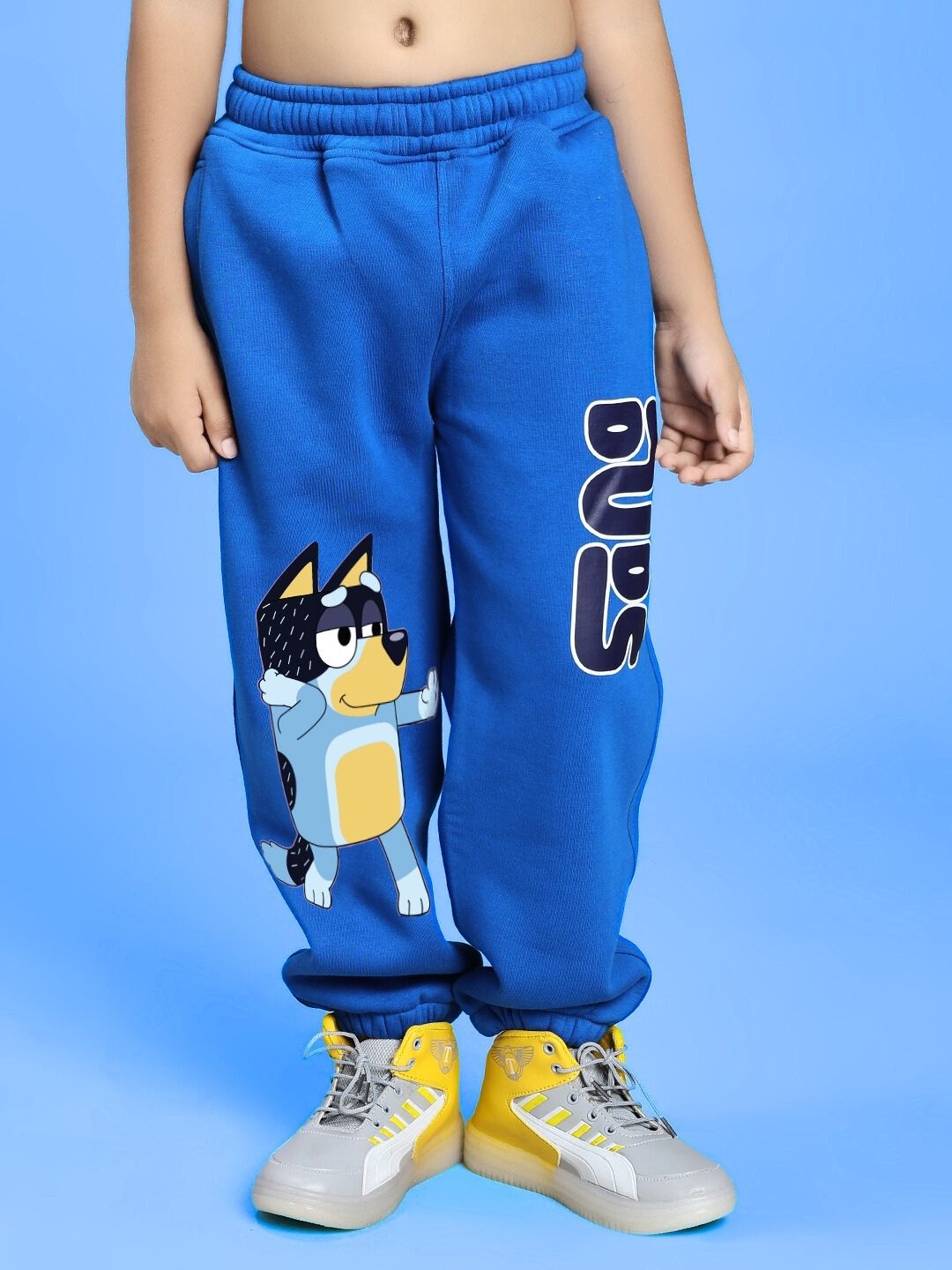 Child wearing BLUEY BINGO FLEECE JOGGER FOR BOYS AND GIRLS BLUE with Bluey character design on a light blue background.