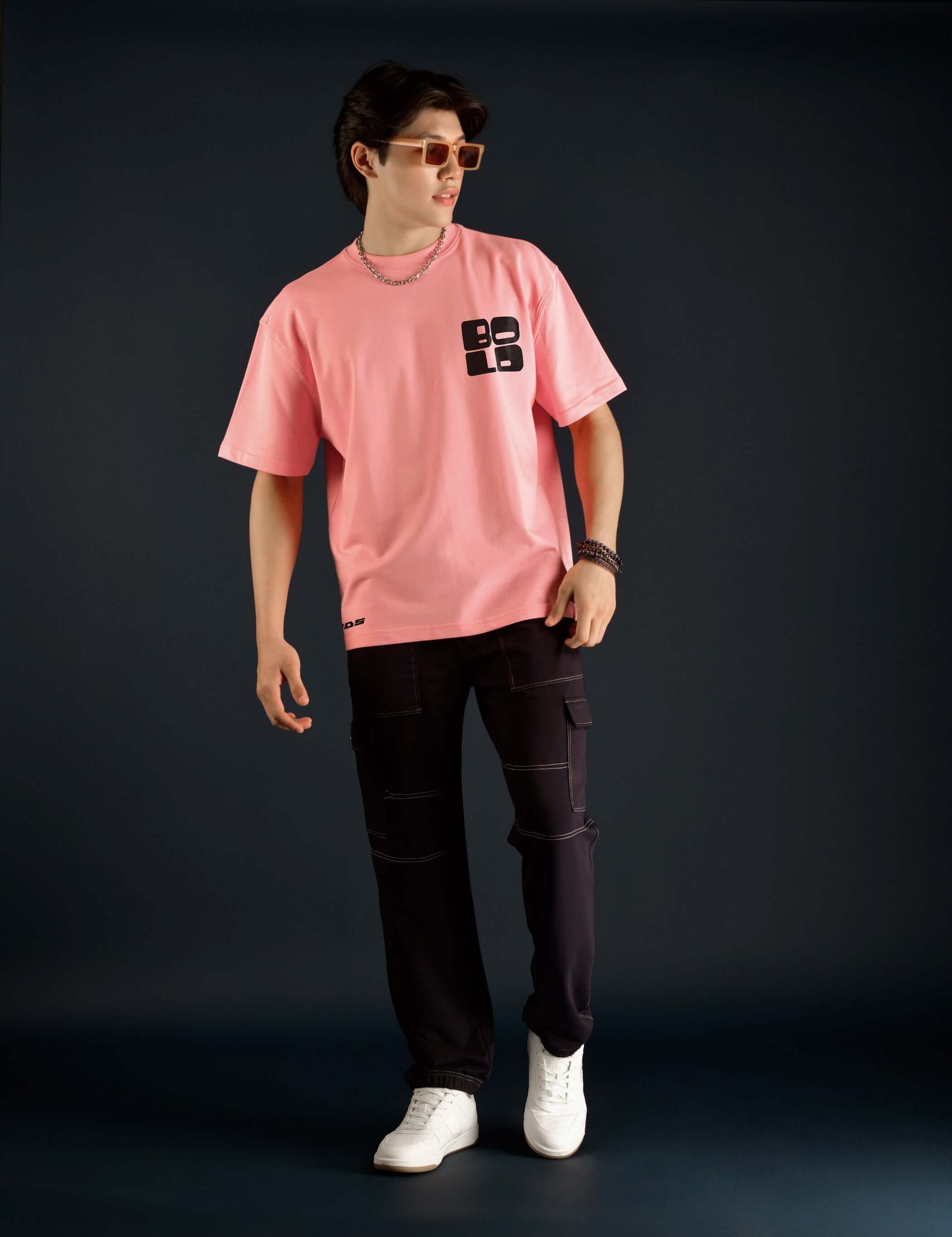 Model wearing a bold over-sized baby pink t-shirt made from premium cotton and elastane, paired with dark pants and sneakers, perfect for casual style.
