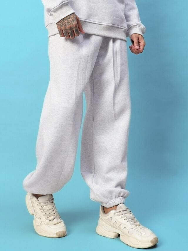 Man wearing Bona-Fide Fleece Pant in melange grey with white sneakers against blue background