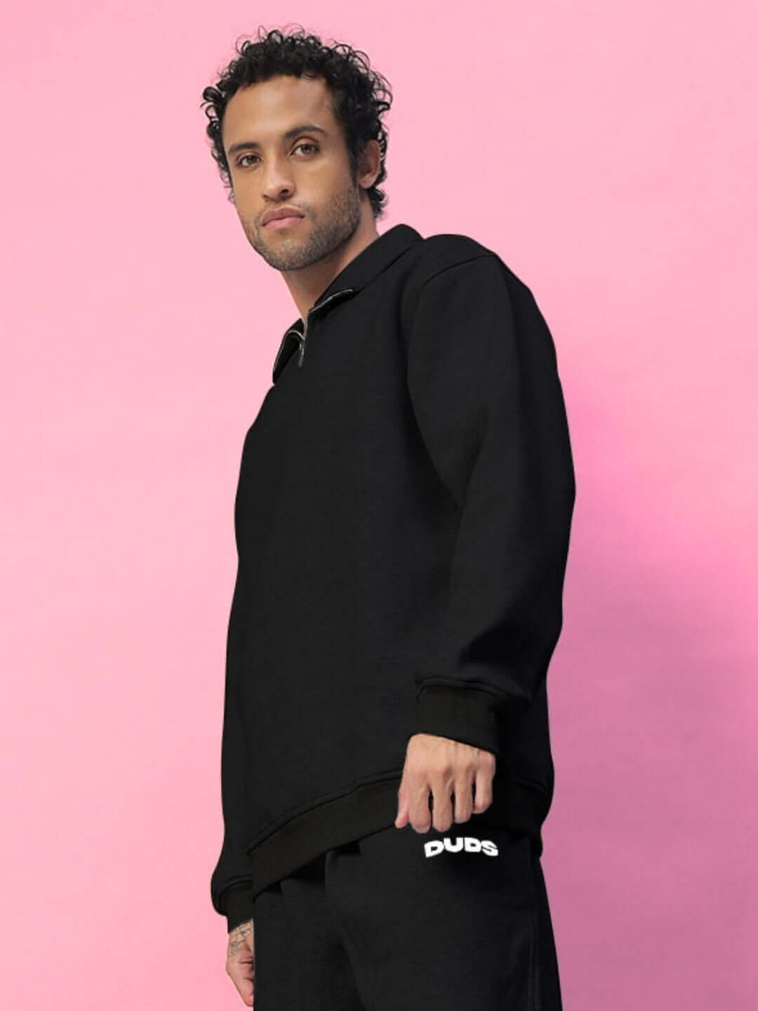 Man wearing BONA-FIDE fleece sweatshirt in black, posing against a pink background.