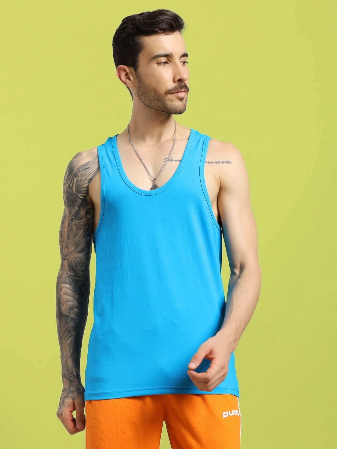 Man wearing a bright blue Bonny Gym T-shirt and orange shorts by DUDS, showcasing activewear fit, with a green background.